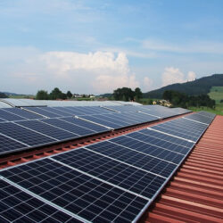 Solar panels on a red roof with a scenic background of hills and trees under a partly cloudy sky.