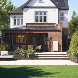 The garden of a modern house, with brickwork. A Tesla Powerwall is affixed to a wall.