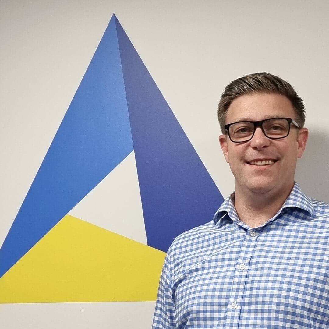 A person wearing glasses and a checkered shirt is standing next to a geometric blue and yellow wall art.