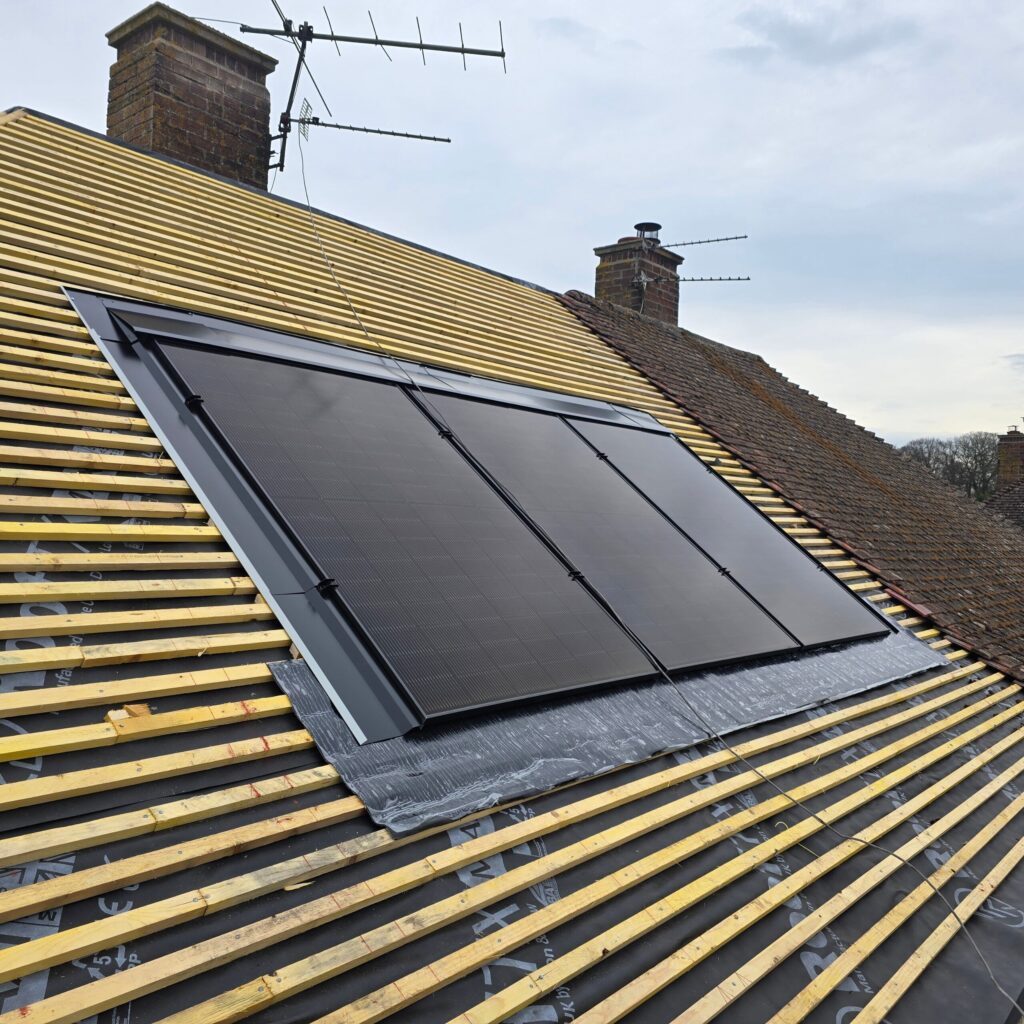 Four black solar panels are mounted on a sloped roof under construction, with exposed wooden battens and roof coverings visible.